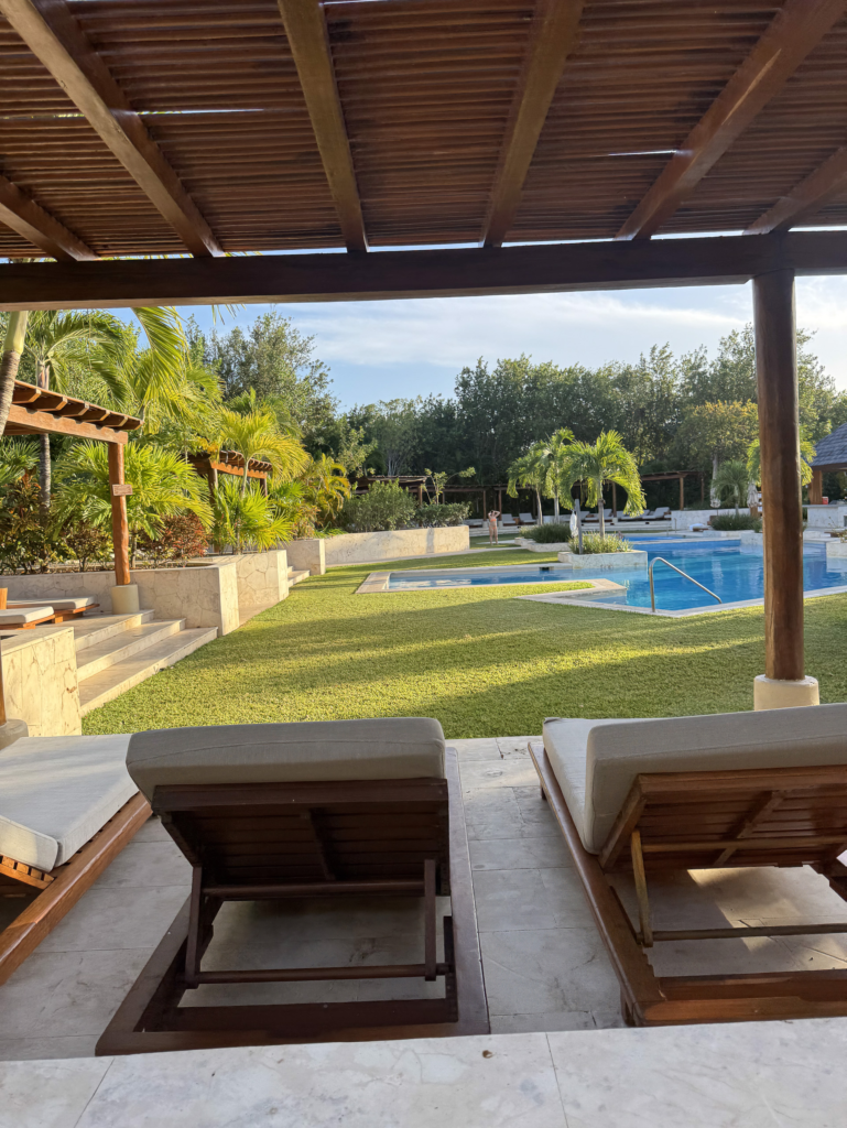 Two wooden loungers under a timber pergola looking across lawn to the resort pool