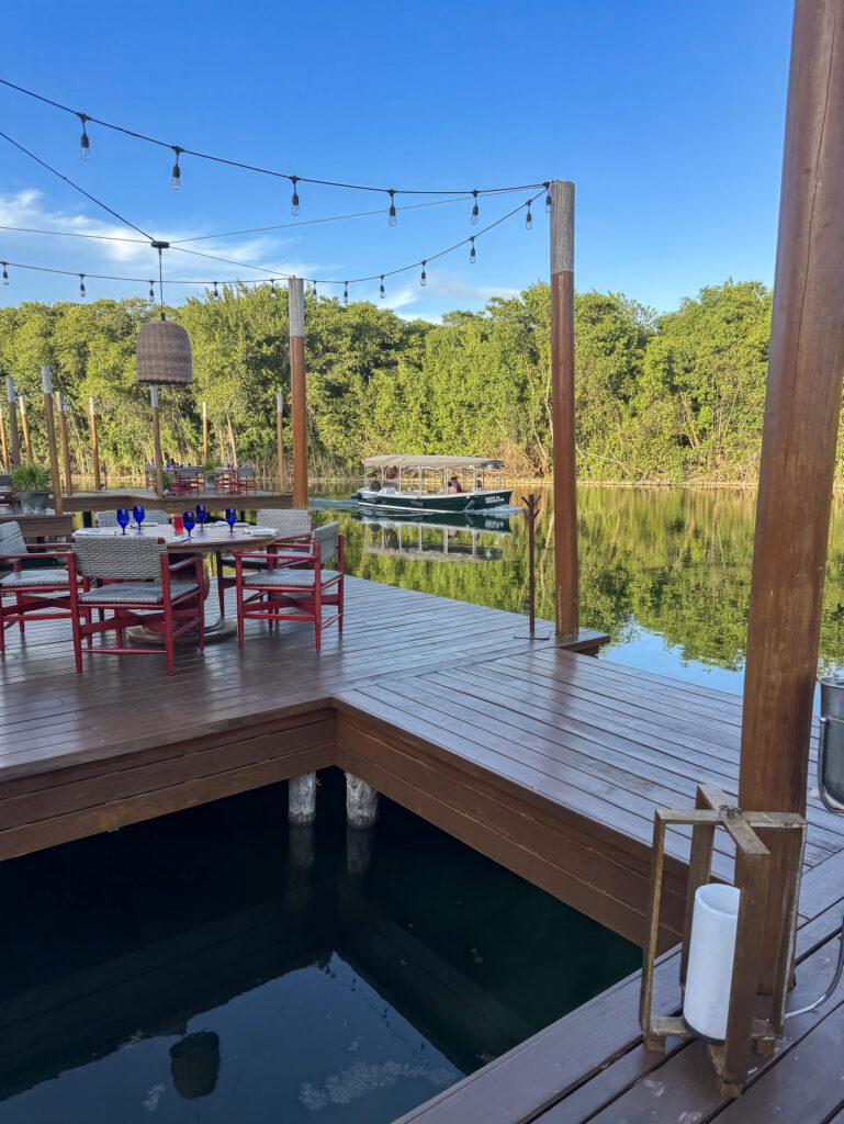 A wooden restaurant deck over the canal set with red chairs and festoon lights, a boat passing behind