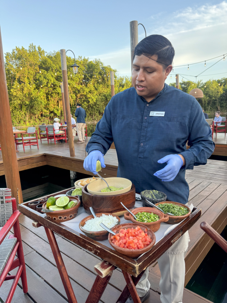 A waiter spooning guacamole from a tableside trolley set with lime, tomato, cheese and chapulines