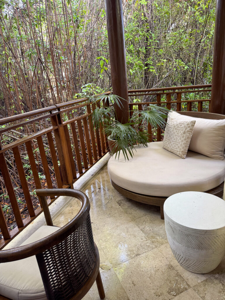 A round cushioned daybed and wicker chair on a casita terrace looking straight into the mangrove