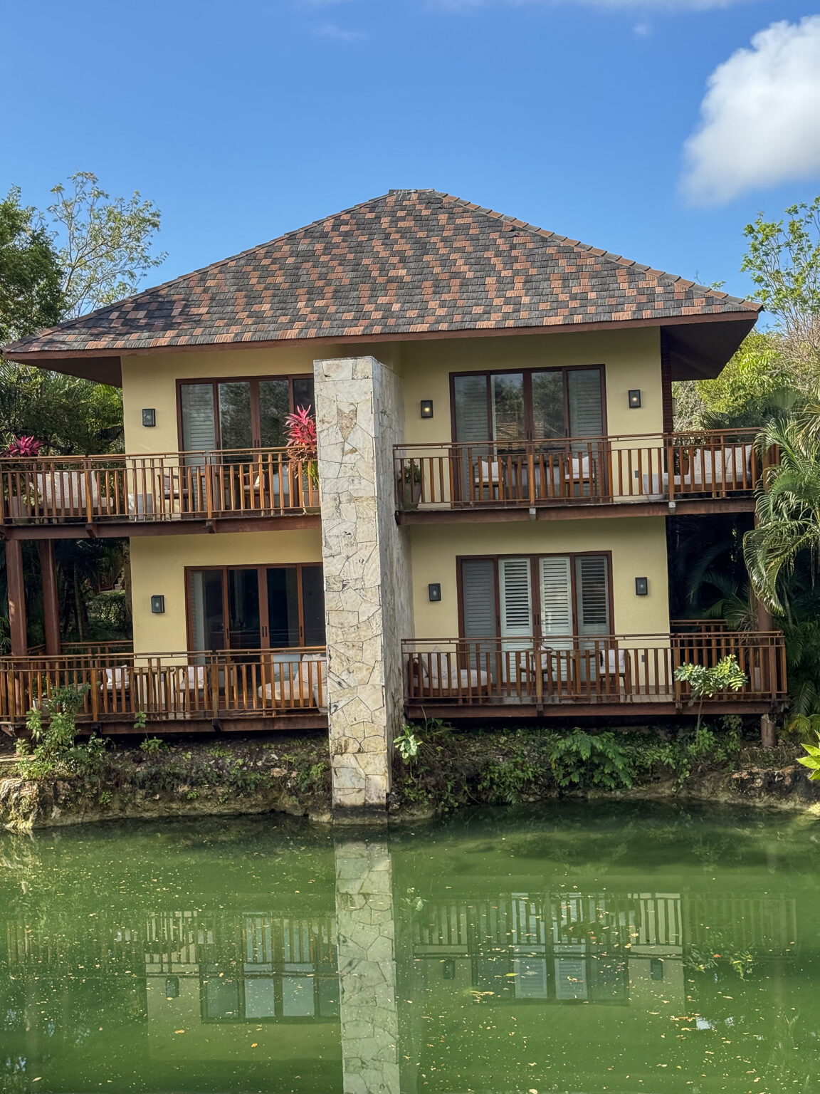 A two-storey casita of pale stucco and wooden balconies standing directly above the green lagoon