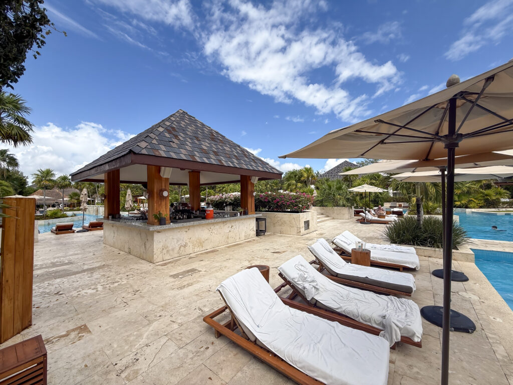 Loungers and canvas umbrellas lined along the main pool with the shingled pool bar behind