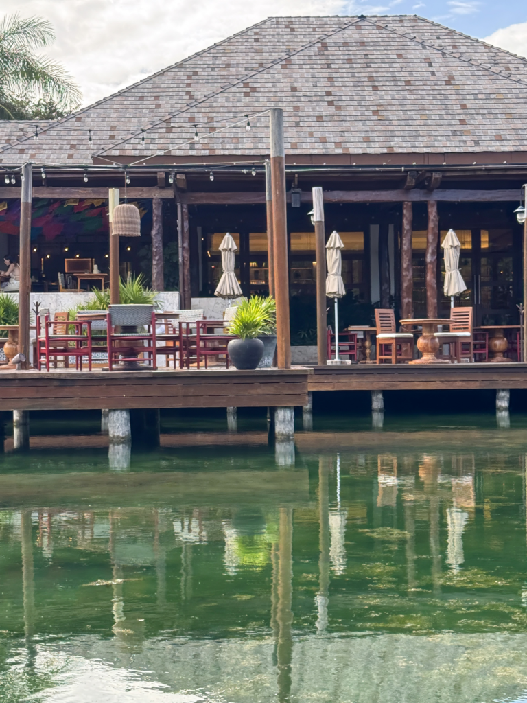 A shingle-roofed restaurant on stilts over the lagoon with red chairs