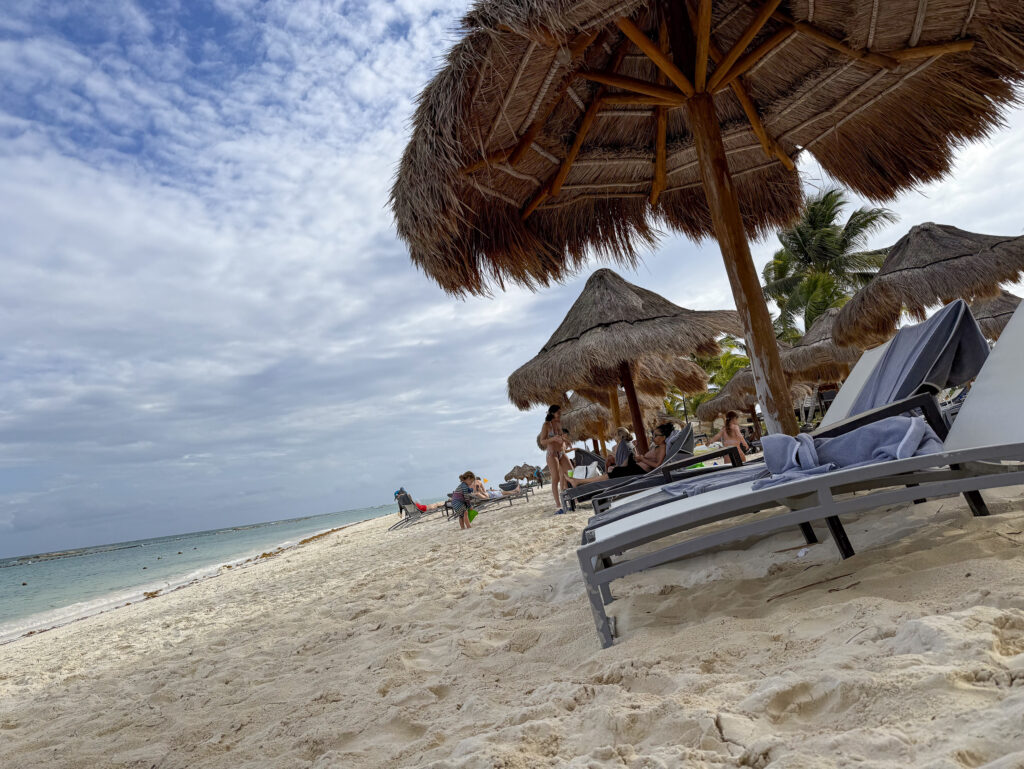Thatched palapas and a lounger on white sand with the Caribbean beyond at Fairmont Mayakoba