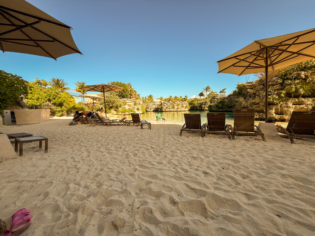 Cream umbrellas and loungers on the sand of a sheltered cove ringed by limestone rock