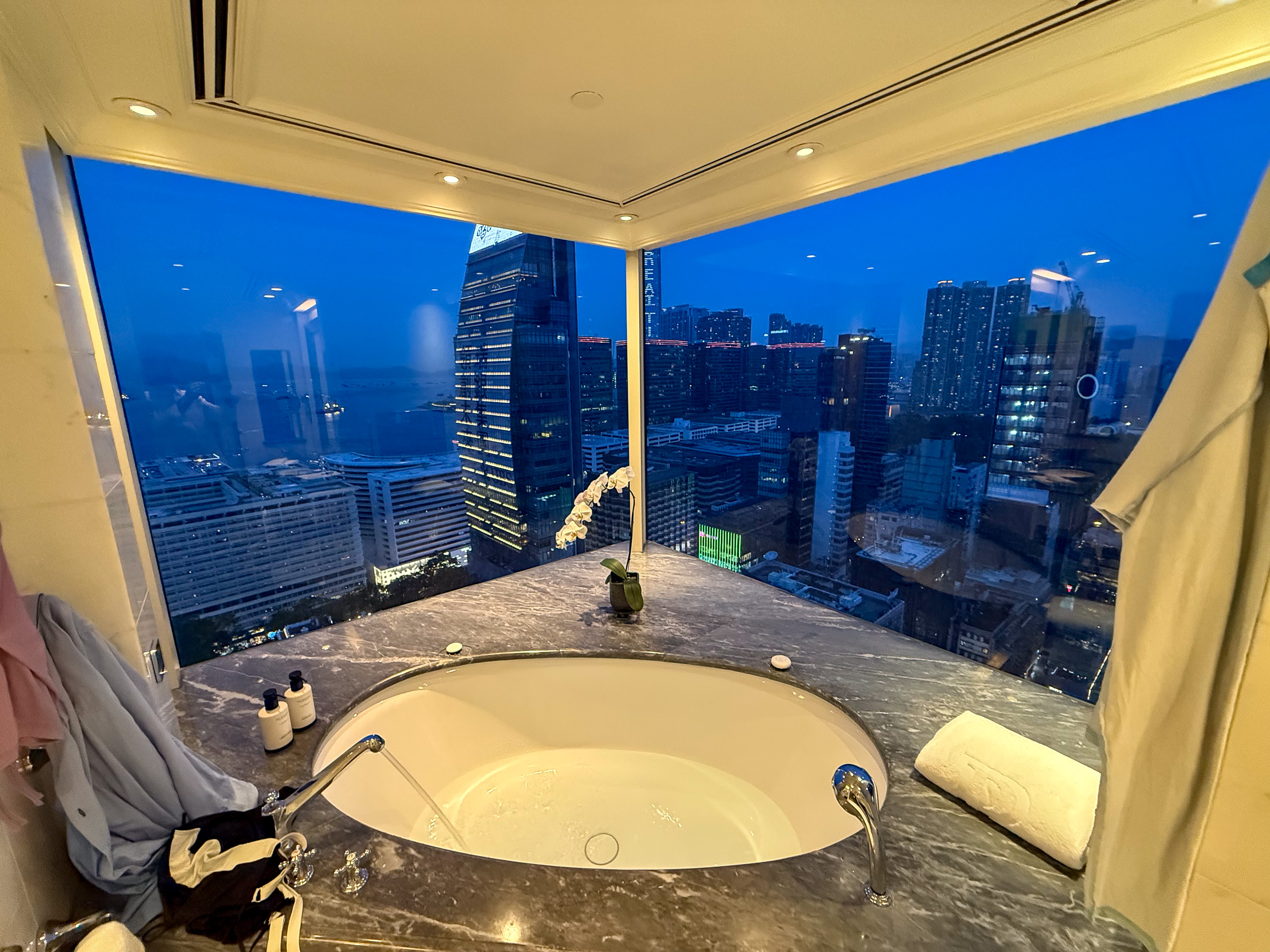 A bathtub set against a floor-to-ceiling window with the Hong Kong skyline at dusk