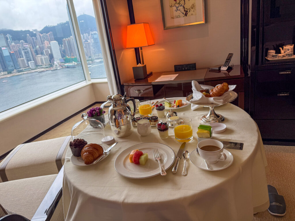 Room-service breakfast on a round table by the window, croissants, coffee and the harbour behind