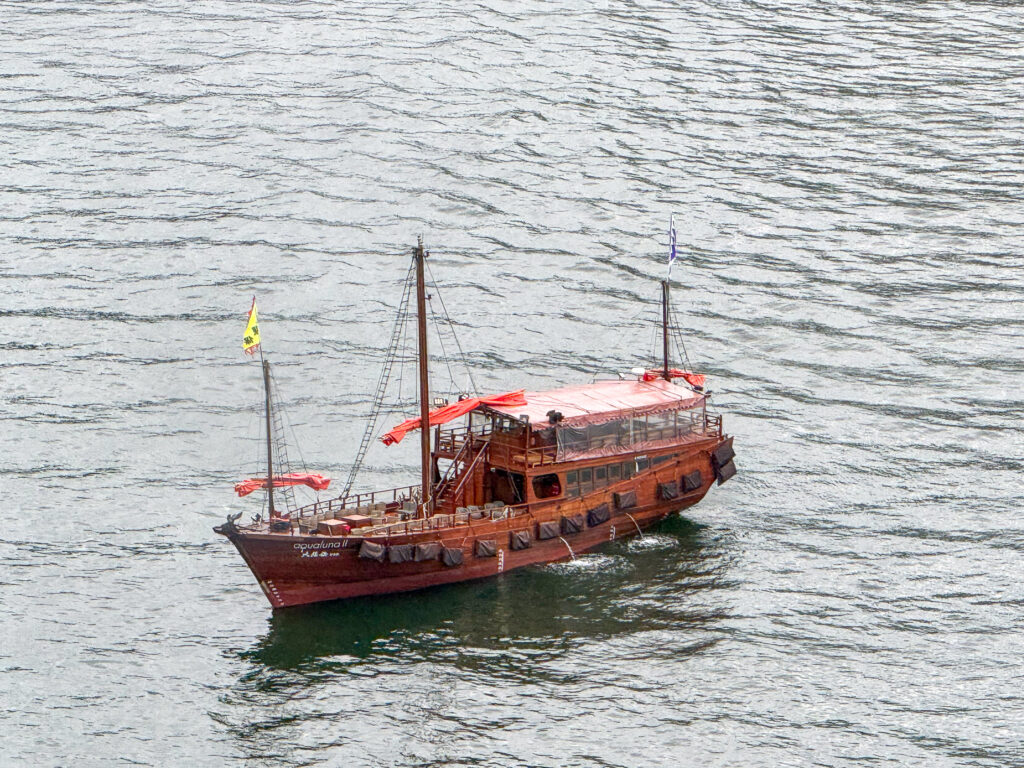 A red-sailed wooden junk crossing the grey water of Victoria Harbour