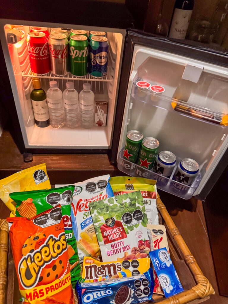 Open minibar of soft drinks, beer, water and wine above a basket of crisps and sweets