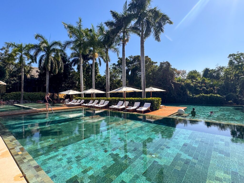 Emerald mosaic-tiled pool reflecting royal palms, with loungers and umbrellas along the far edge