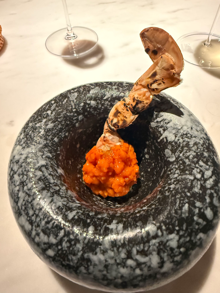 A mound of bright orange roe with a charred prawn tail arching out of it in a speckled black stone bowl