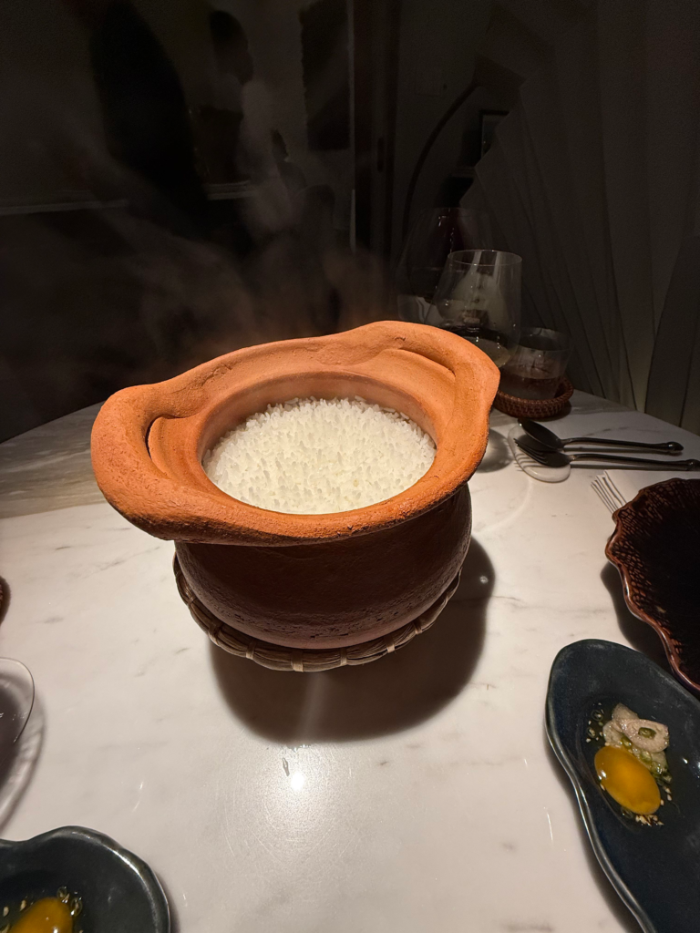 A terracotta pot of steaming jasmine rice set in a woven basket on the marble table