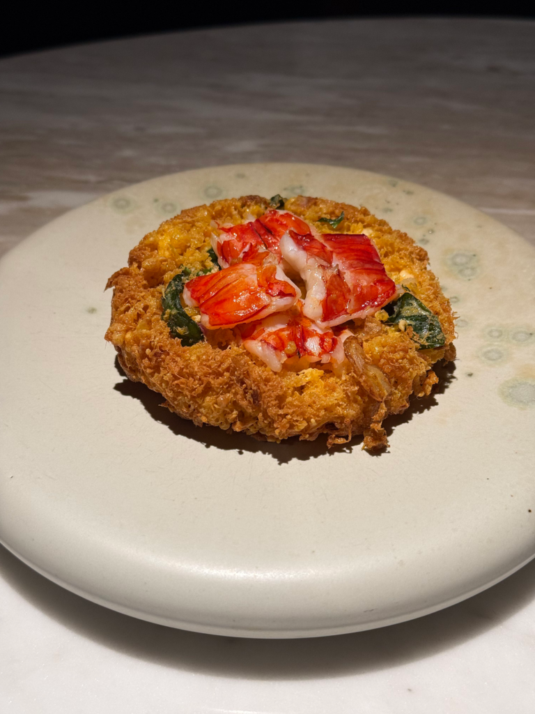 A crisp golden omelette ringed around chunks of lobster meat and greens on a pale ceramic plate