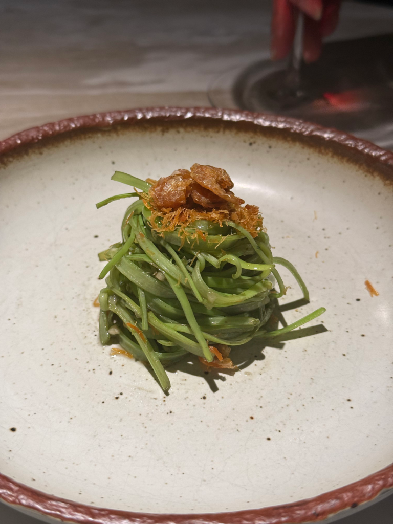A tangle of stir-fried morning glory crowned with crisp fried garlic and shallots in a rustic bowl