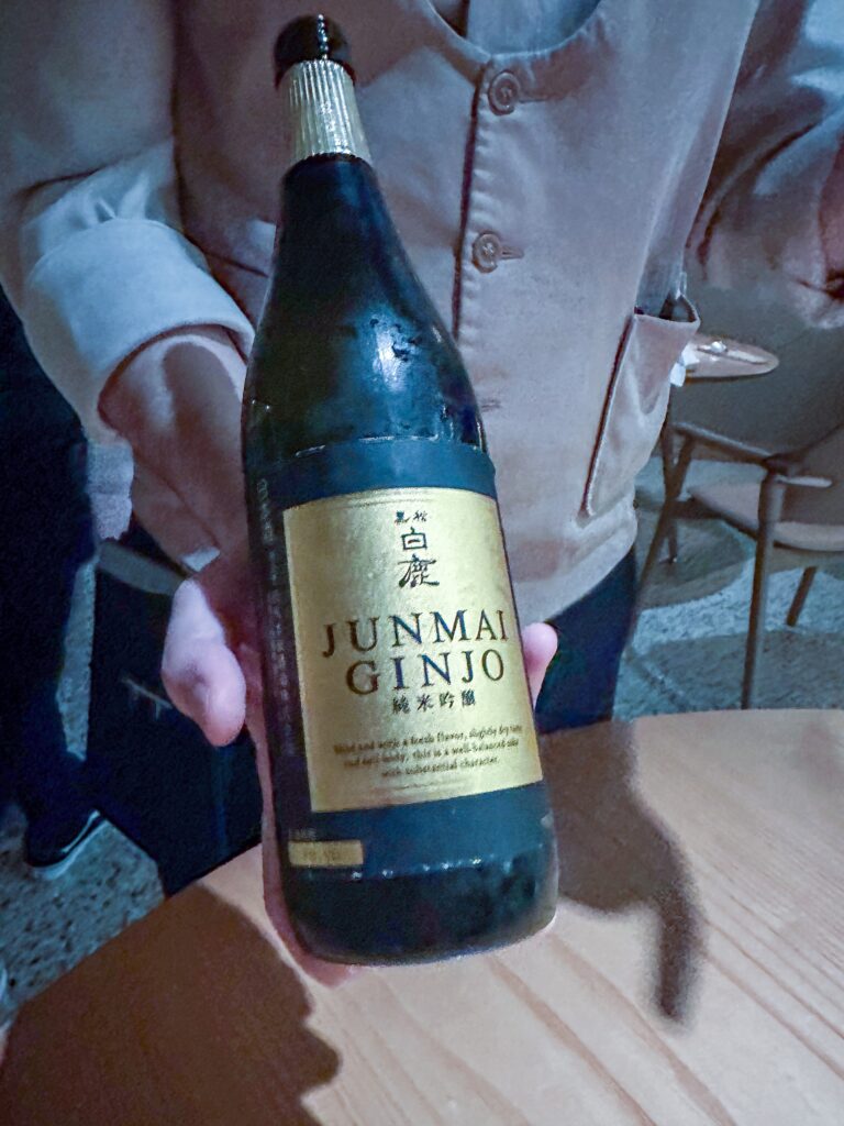 A sommelier holding a bottle of Junmai Ginjo sake with a gold label