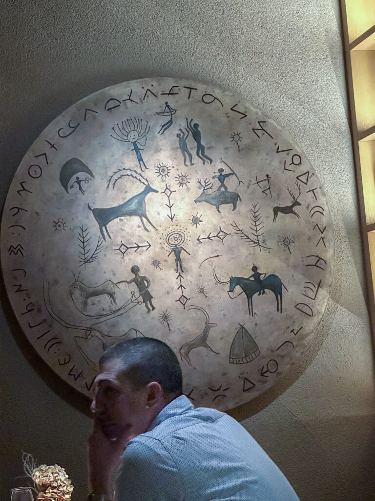 A diner seated beneath the large round wall disc painted with Anatolian rock-art figures and runic script