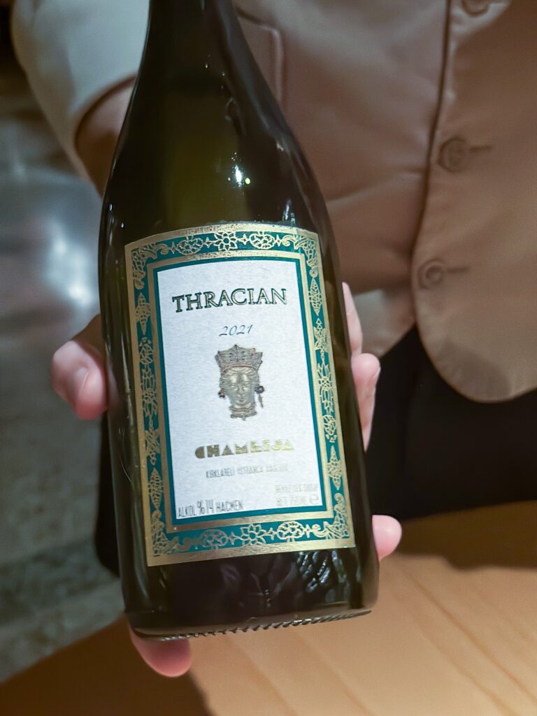A hand holding a bottle of Chamlija Thracian white wine with a turquoise and gold label