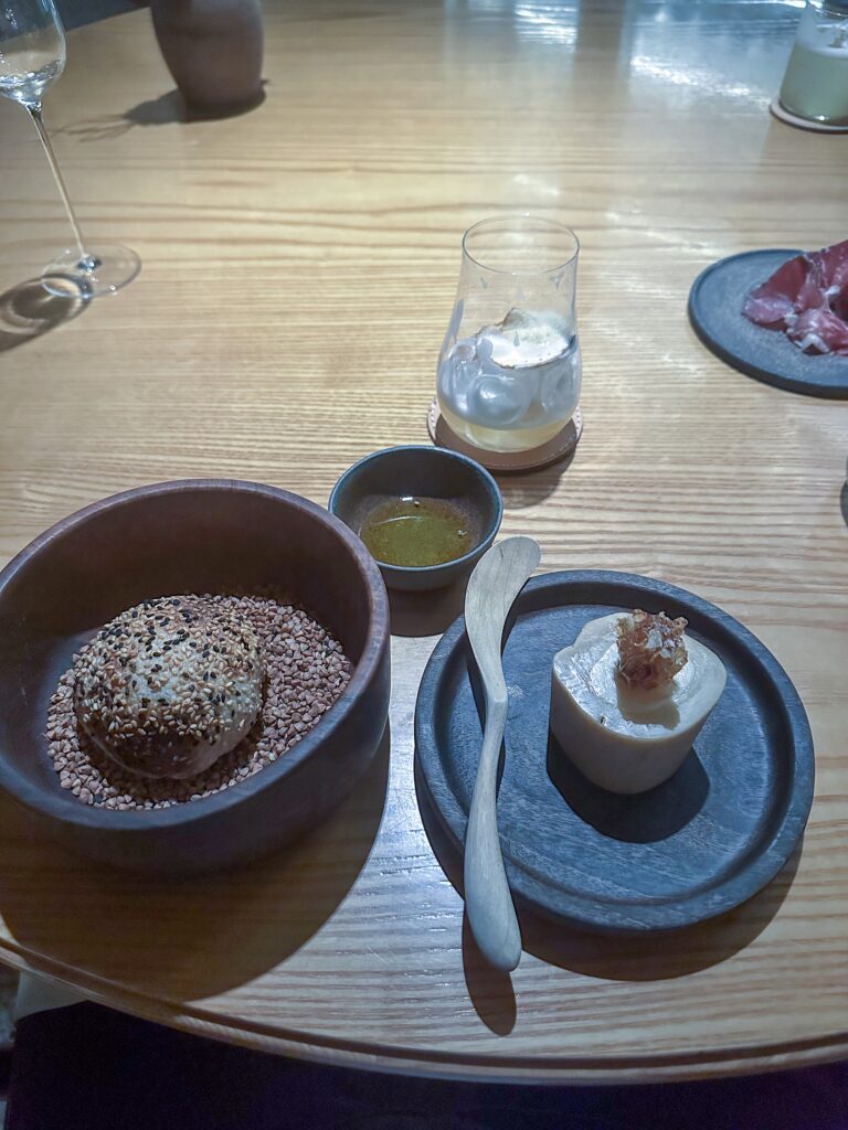 The bread course: a sesame-crusted roll in a bowl of buckwheat, a cylinder of cheese on a slate dish, olive oil and a wooden spreader