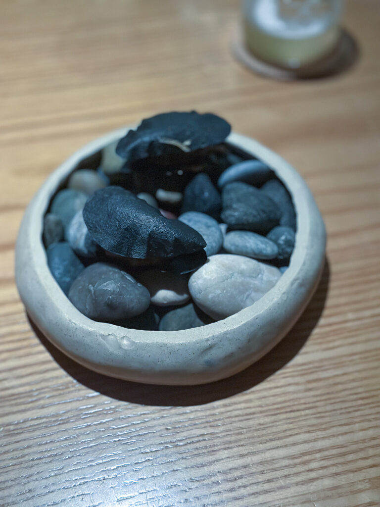 A dish disguised as river stones, dark shapes set among grey pebbles in a stone bowl