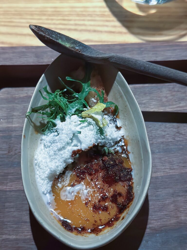 A bruleed custard under a drift of grated white cheese and a curl of green herb in an oval dish