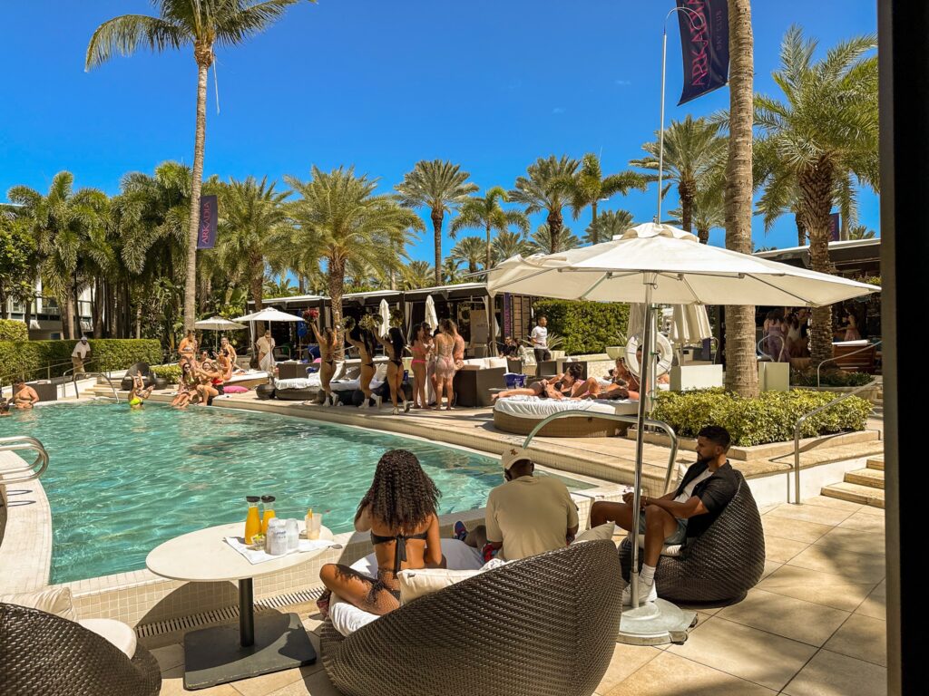 Afternoon pool party at the adults pool, guests on daybeds and wicker chairs under palms and umbrellas