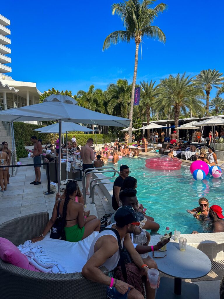 Poolside daybeds and inflatable rings around the party pool beneath a single tall palm