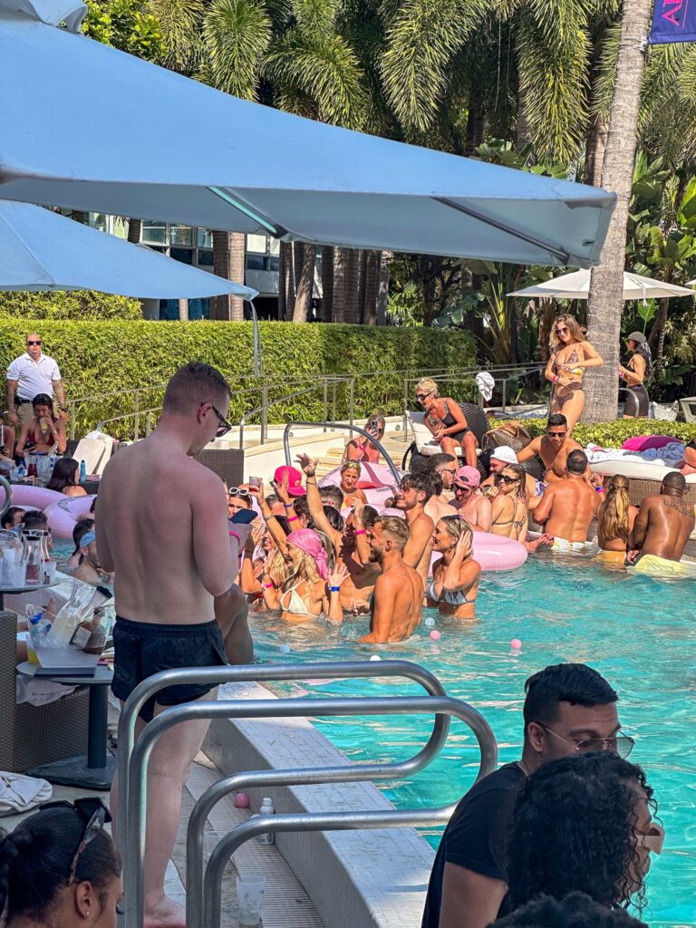 Guests gathered in the shallow end of the pool during an afternoon party, cabanas behind