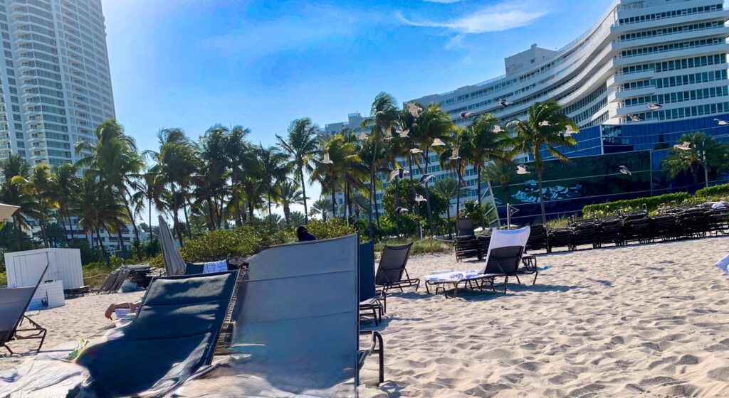 Beach loungers with privacy screens on the sand, looking back at the curved Chateau tower
