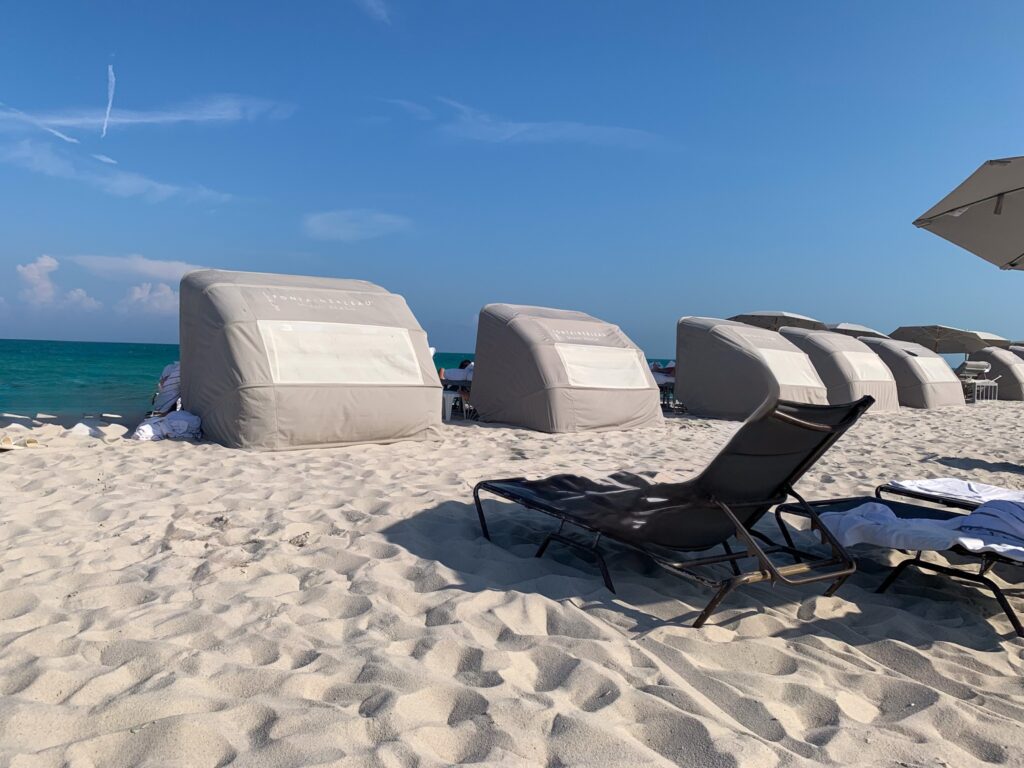 Row of canvas beach cabanas and a lounger on the sand beside the calm ocean