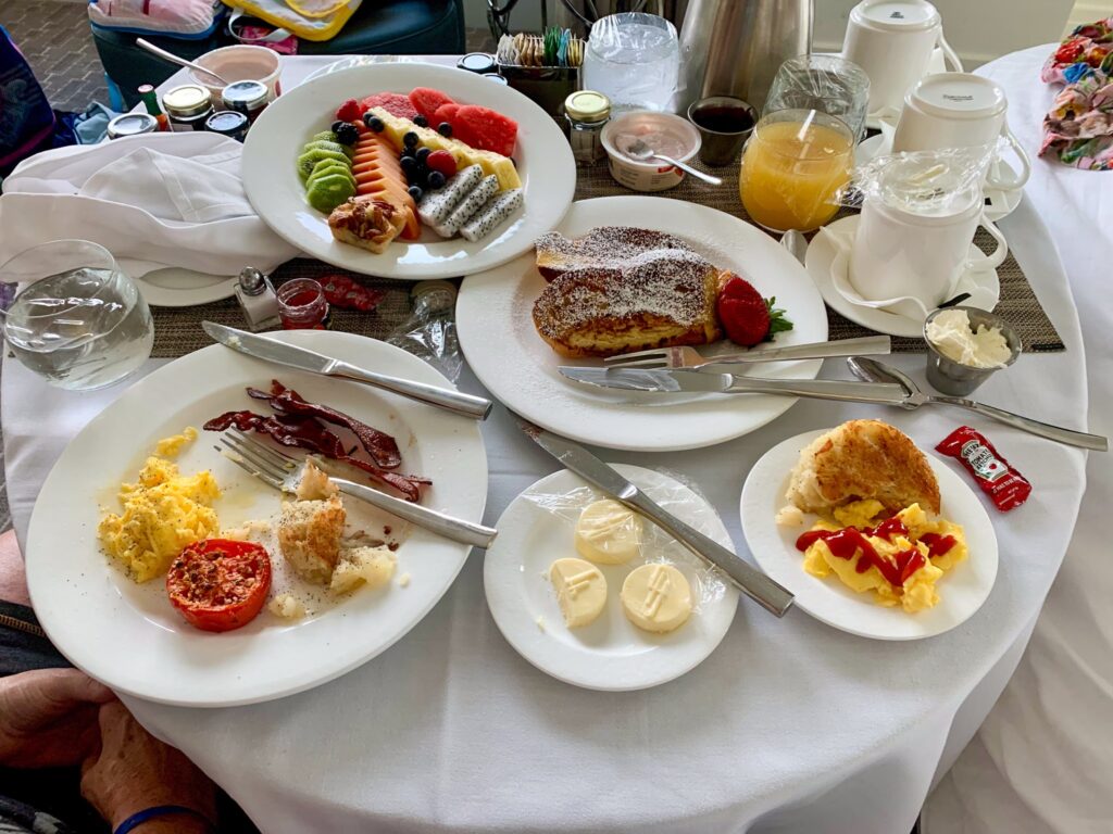 Room service breakfast of eggs, French toast, fruit and pastries on a white clothed table