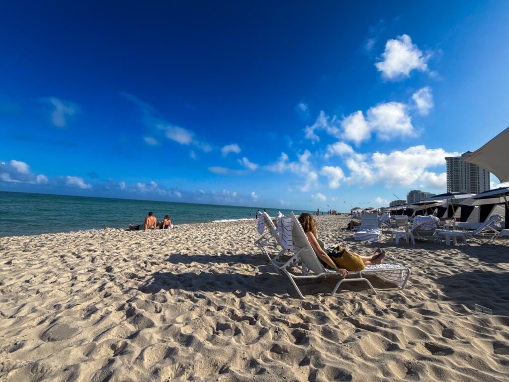 A guest reading on a beach chair on the wide sand with the ocean and skyline beyond