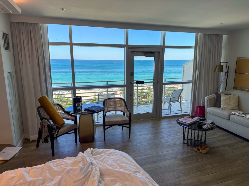 Oceanfront room with mid century chairs, writing table and sliding doors onto the balcony