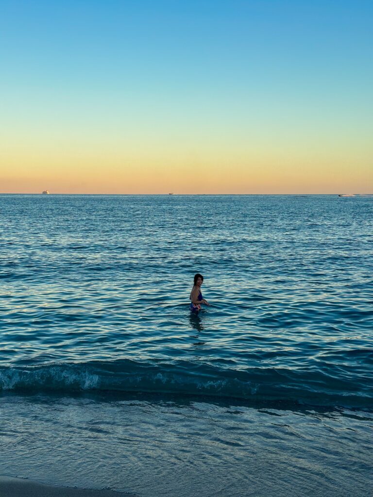 A swimmer standing in calm water at dusk with the horizon glowing gold