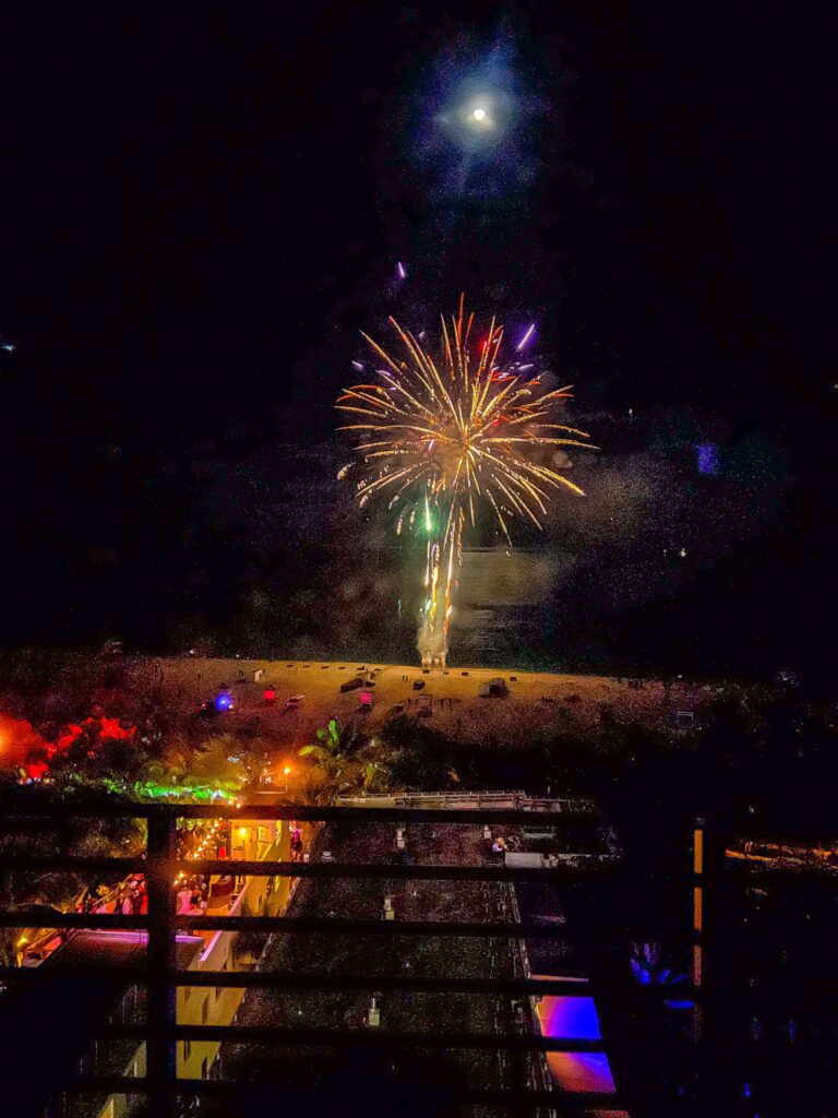 Fireworks bursting over the beach at night under a full moon
