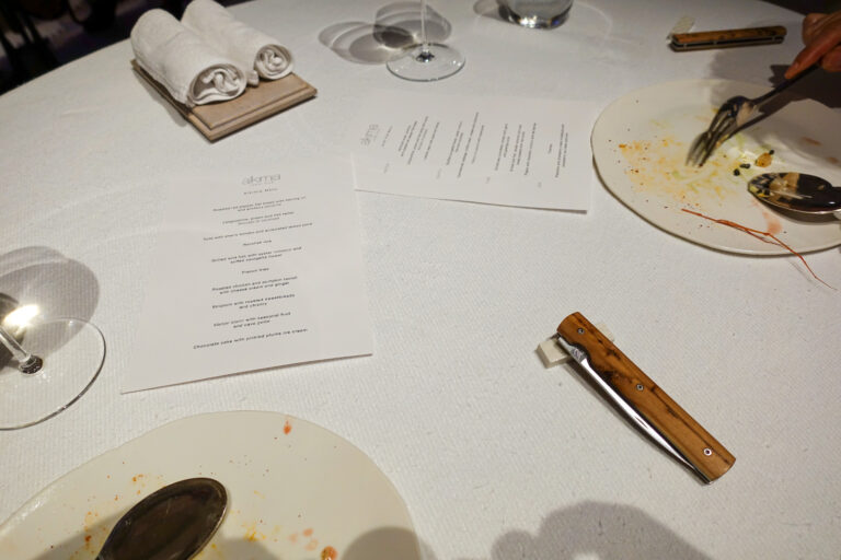 The table between courses, spent shells and the printed menu beside a wooden-handled knife on white linen