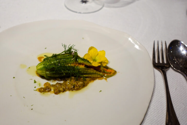 A stuffed courgette flower with its blossom intact, set on a chunky herb sauce