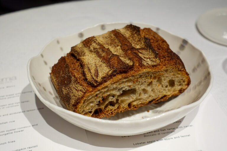 A scored country loaf in a shallow white dish, resting on the printed menu