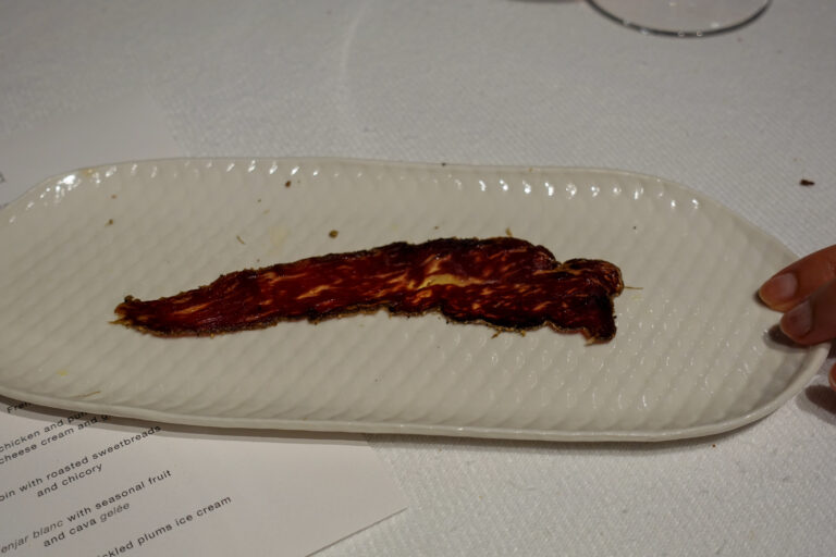 A long dark strip of glazed flat bread laid across a narrow oval plate, the menu beneath