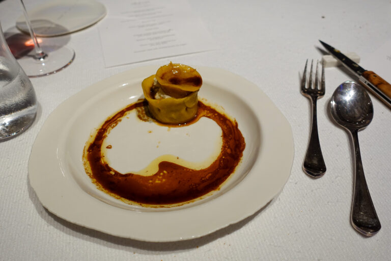 A single filled pasta set inside a ring of dark sauce on a shallow white plate