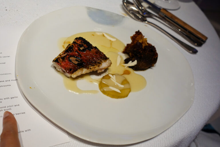 A charred fillet with a pale sauce and a dark garnish, the menu just in frame at the edge of the table