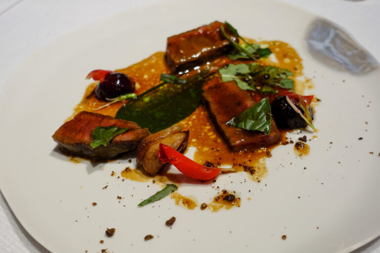 Sliced meat glazed in its own juices with herbs and peppers across a wide white plate