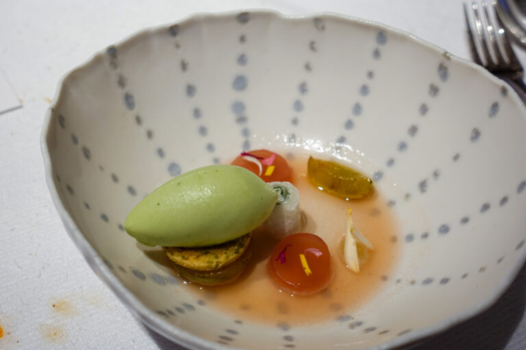 A quenelle of green sorbet with peeled cherry tomatoes in a broth, served in a blue-spotted bowl