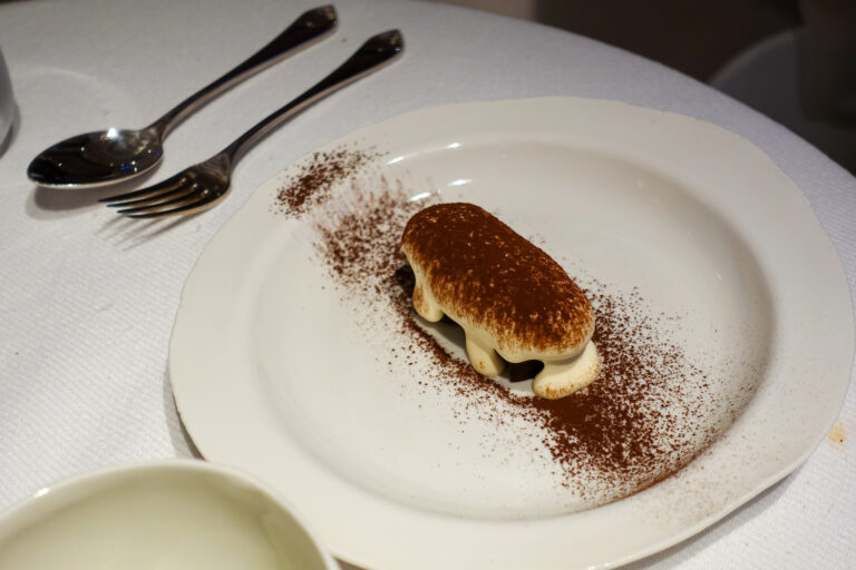An oval of cream and dark fruit under a heavy dusting of cocoa on a white plate