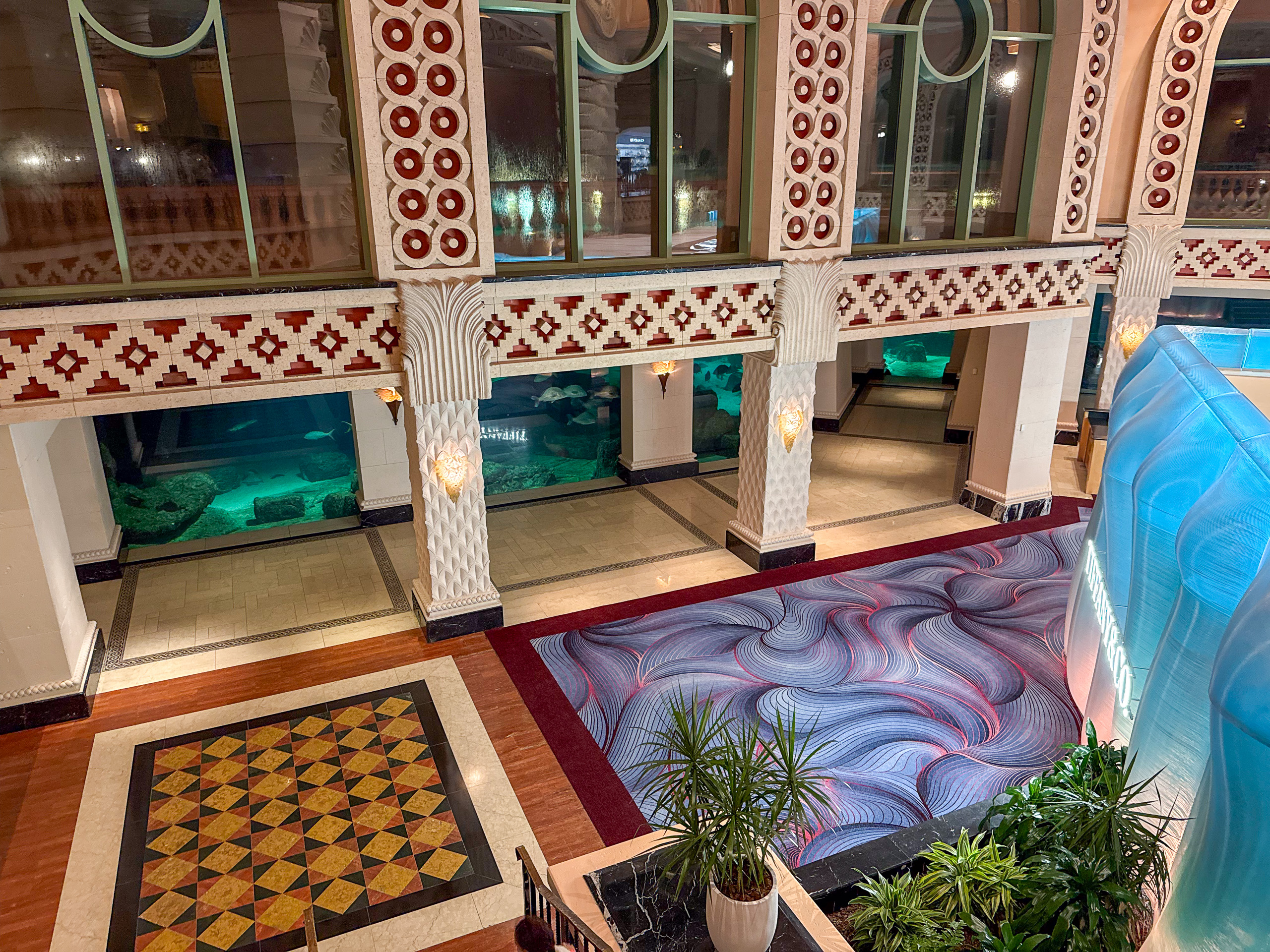 The great hall on the way in: patterned marble, arches, chandeliers, and the aquarium glowing at the far end