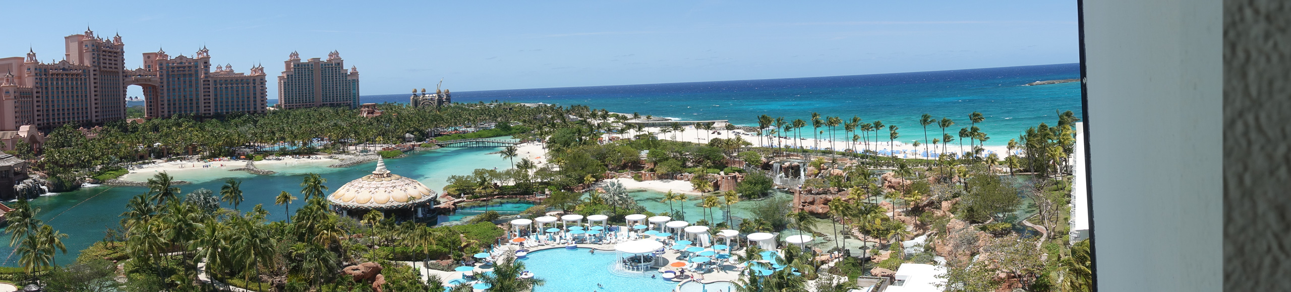 The full sweep of the grounds in one frame: pools, daybeds, palms, then the Atlantic