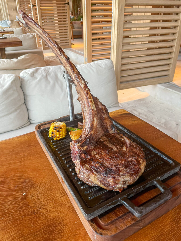 A tomahawk steak on a cast-iron grill plate with charred corn, served on a low table in the lounge