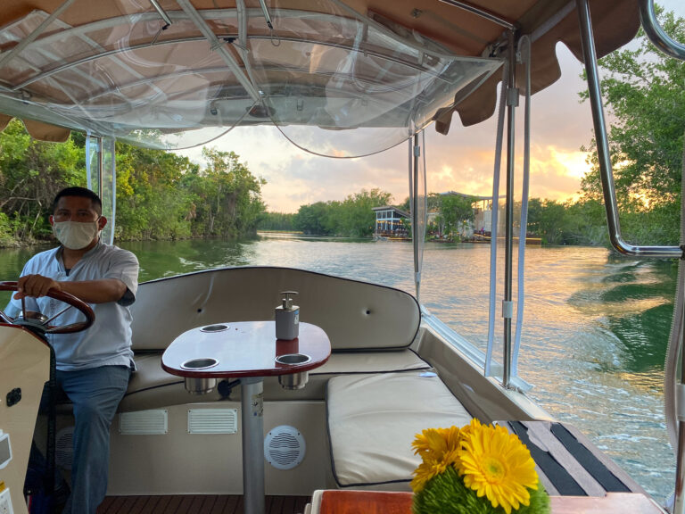 The boatman steering the covered launch along the lagoon at dusk