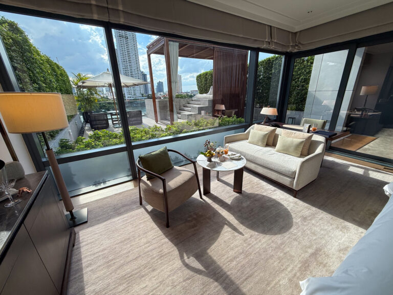 A corner living room glazed on two sides, sofa and armchair facing the terrace planting