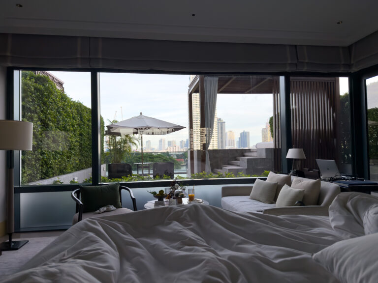 Looking from the unmade bed through full-height glass to the terrace and the city