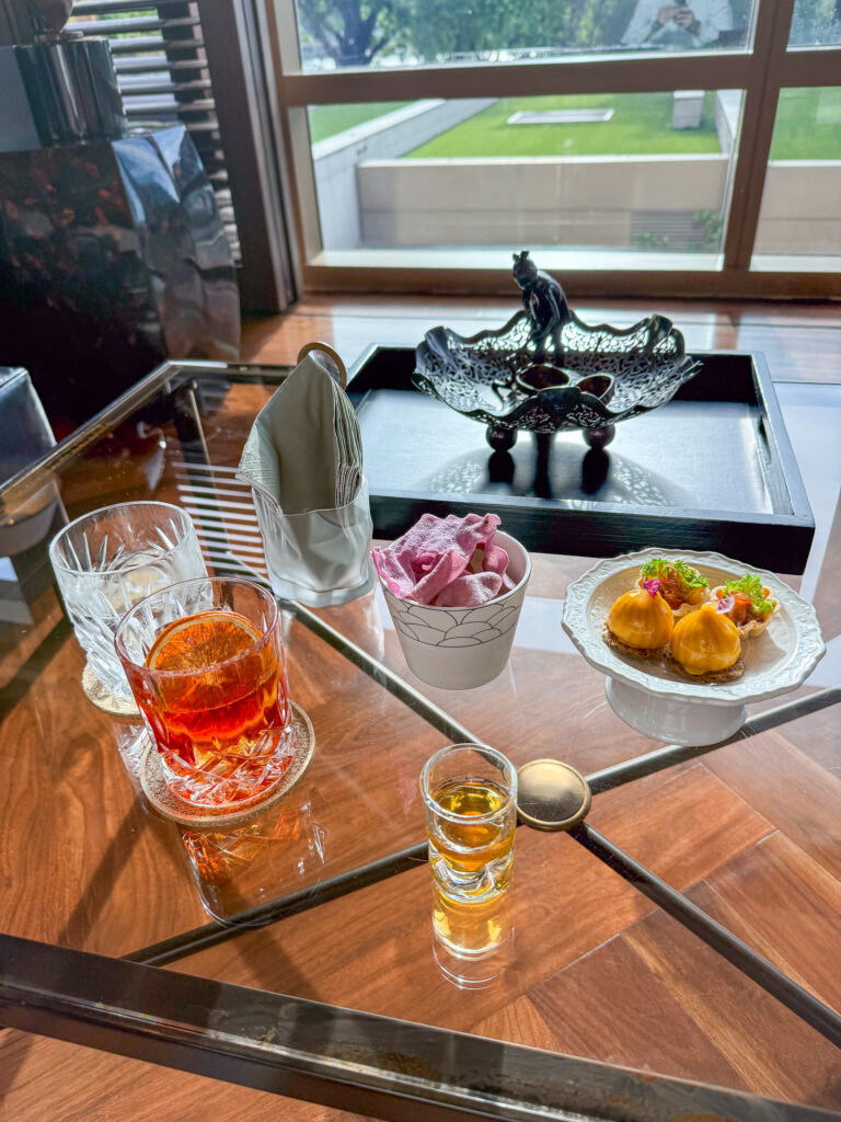Cut glass tumblers of whisky beside dumplings and a bowl of crisps on a mirrored table